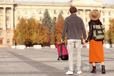 Photo of Couple of travelers with backpacks on city street, back view