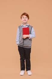 Photo of Smiling schoolboy with book on beige background