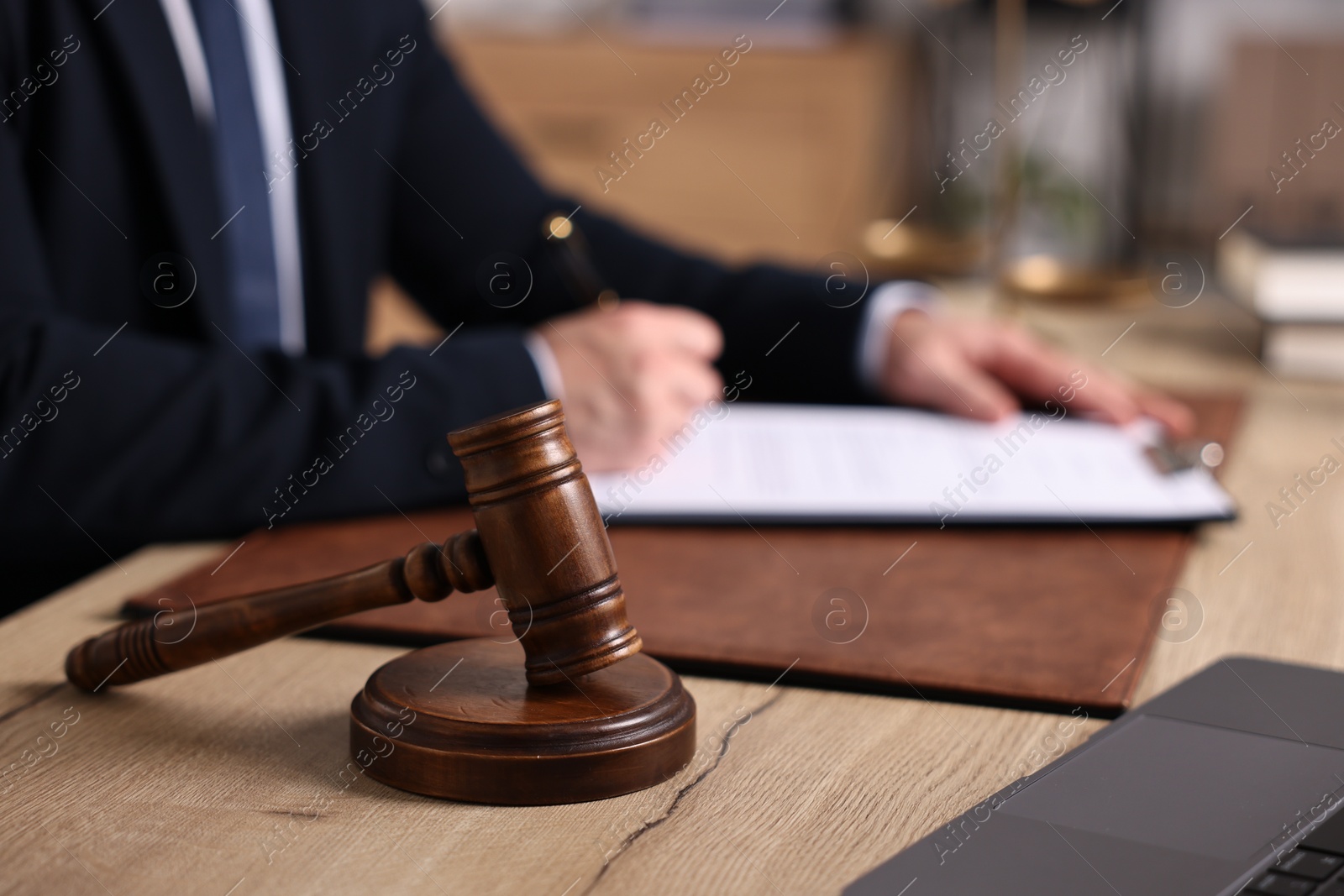 Photo of Notary writing notes at wooden table in office. focus on gavel