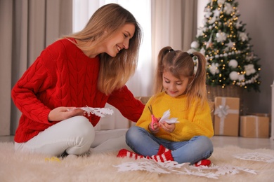 Happy mother and daughter making paper snowflakes near Christmas tree at home