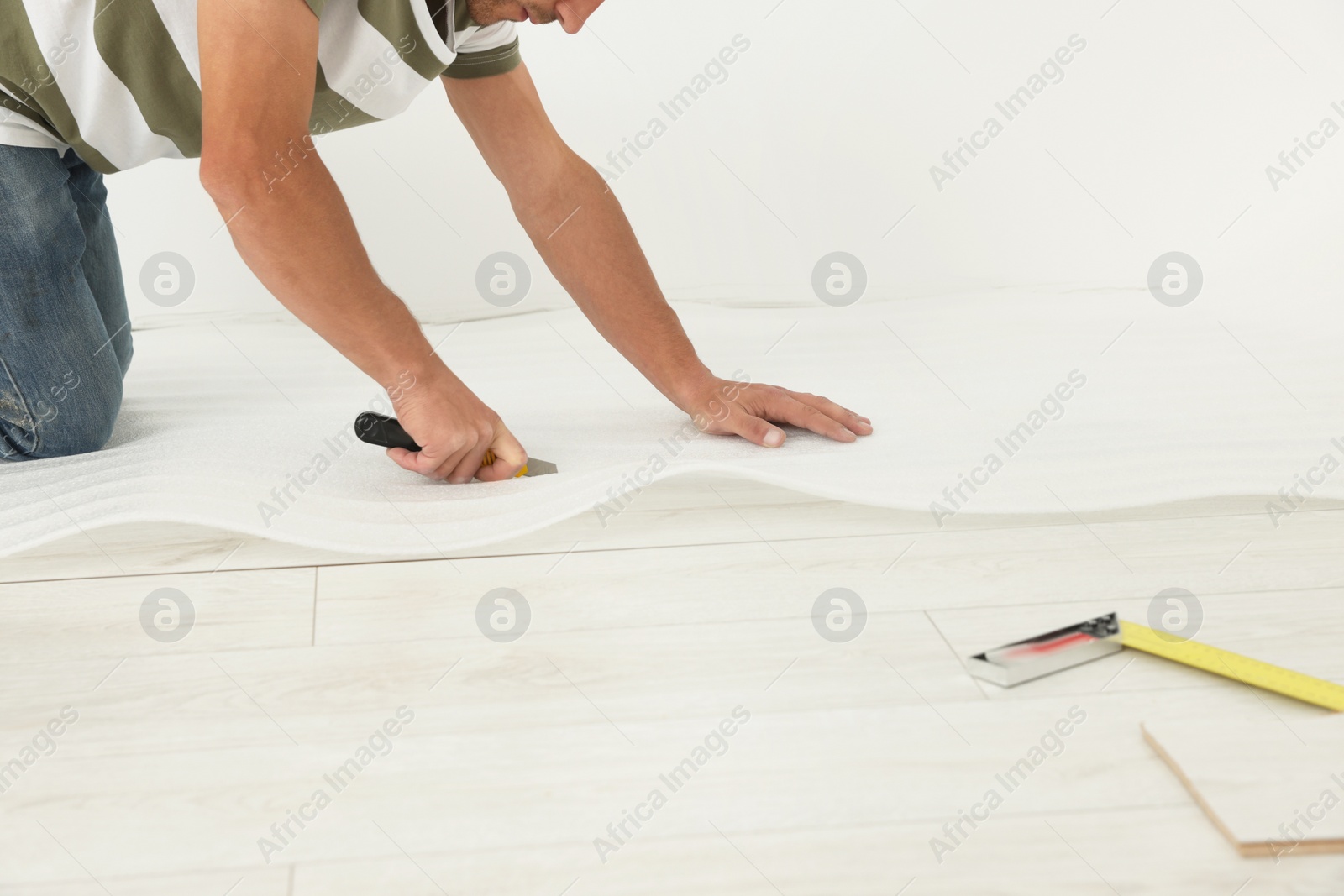 Photo of Professional worker cutting polyethylene foam during installation of laminate flooring indoors, closeup