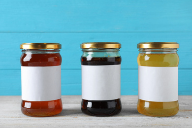Jars of organic honey with blank labels on wooden table against light blue background. Space for text