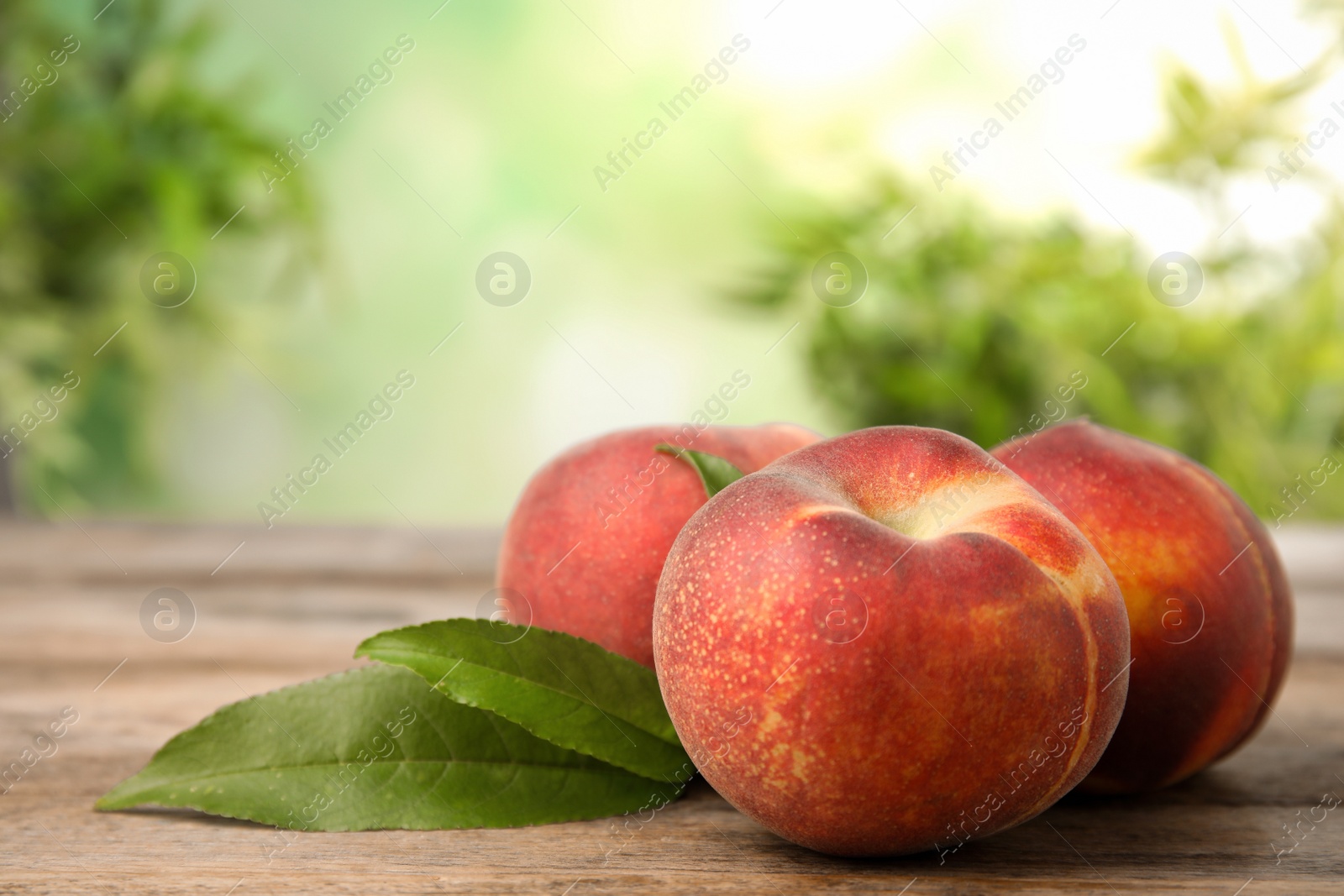 Photo of Fresh peaches and leaves on wooden table against green blurred background, space for text