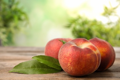 Photo of Fresh peaches and leaves on wooden table against green blurred background, space for text