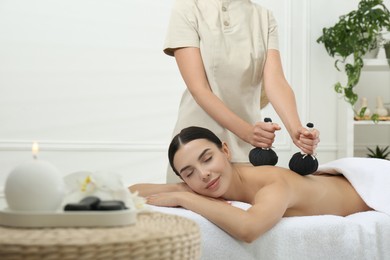 Photo of Young woman receiving herbal bag massage in spa salon