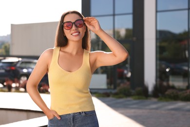 Beautiful smiling woman in sunglasses on city street, space for text