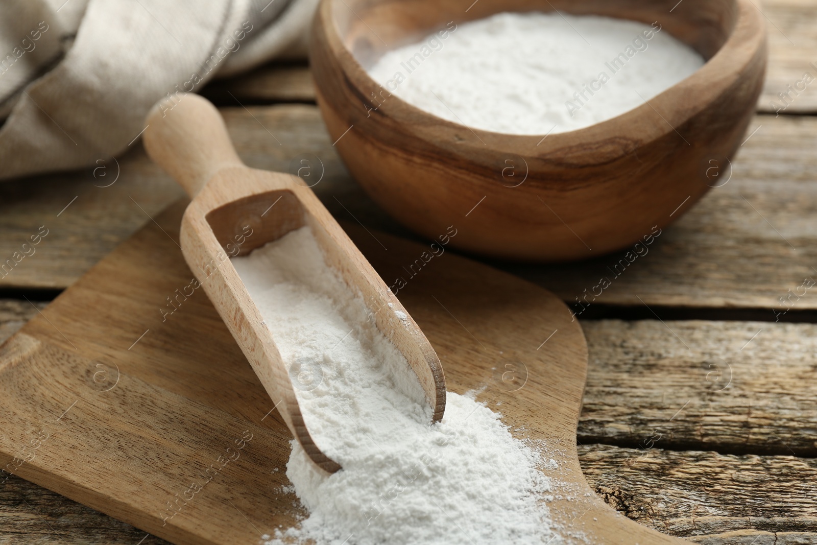 Photo of Baking powder in scoop and bowl on wooden table, closeup