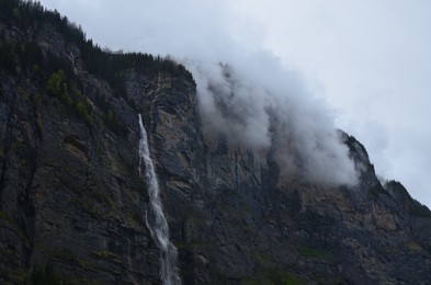 Photo of Picturesque view of waterfall and mountains covered with fog