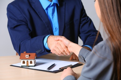 Photo of Woman shaking hands with real estate agent at table in office, closeup. Home insurance