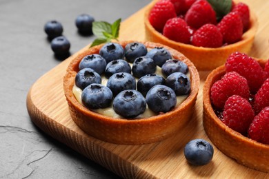 Photo of Tartlets with different fresh berries on black table, closeup. Delicious dessert