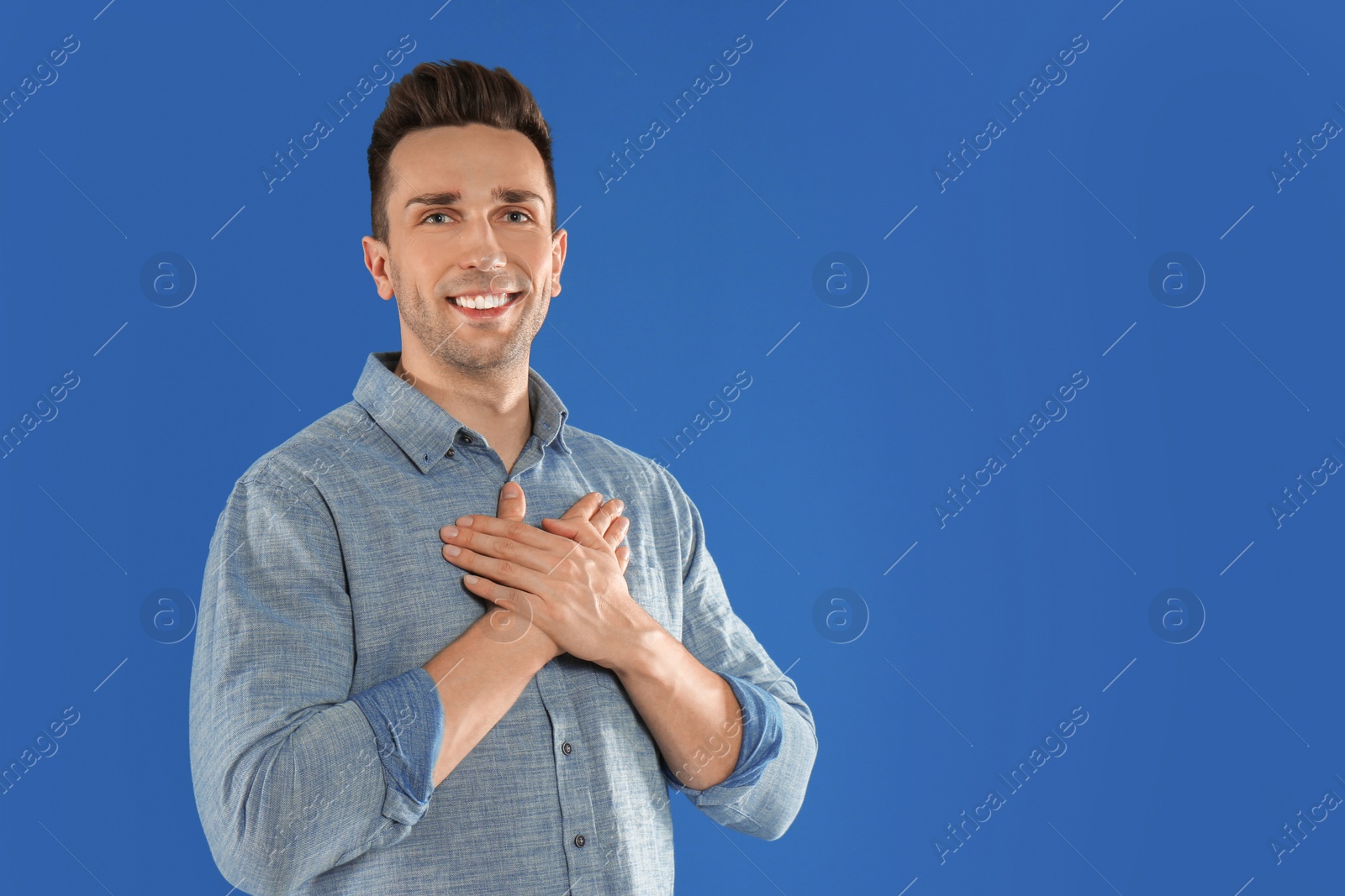 Photo of Handsome grateful man with hands on chest against blue background. Space for text