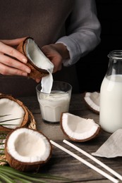 Woman pouring tasty coconut milk into glass at wooden table, closeup
