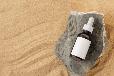 Photo of Bottle of serum and stone on sand, top view. Space for text
