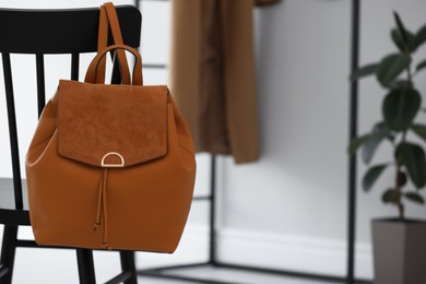 Stylish brown backpack hanging on black chair indoors, space for text