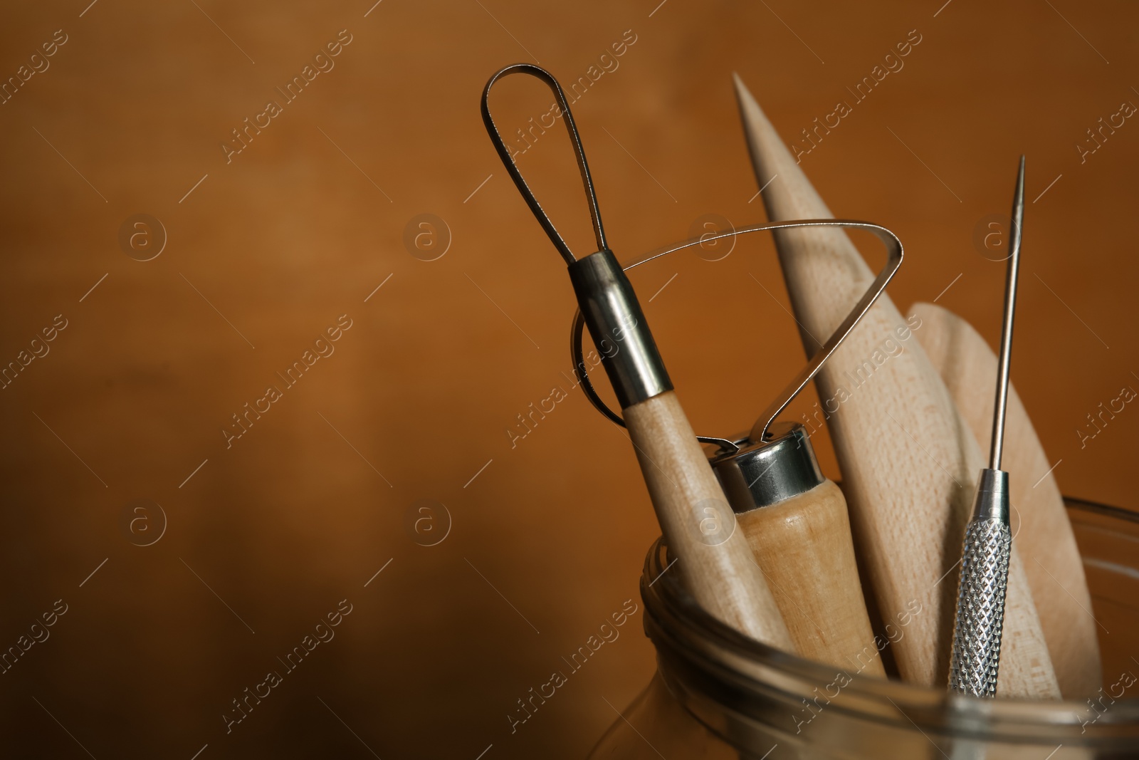 Photo of Set of clay modeling tools in glass jar on brown background, closeup. Space for text