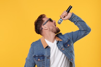 Photo of Handsome man with sunglasses and microphone singing on yellow background