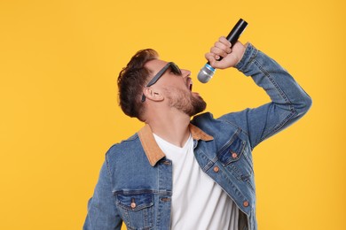 Handsome man with sunglasses and microphone singing on yellow background