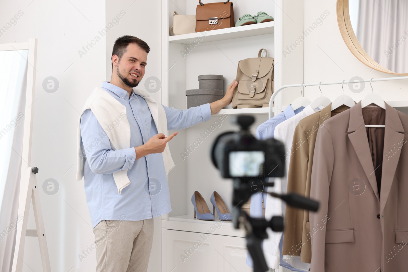 Photo of Smiling fashion blogger showing clothes while recording video at home