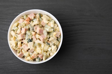Photo of Tasty Olivier salad with boiled sausage in bowl on grey wooden table, top view. Space for text
