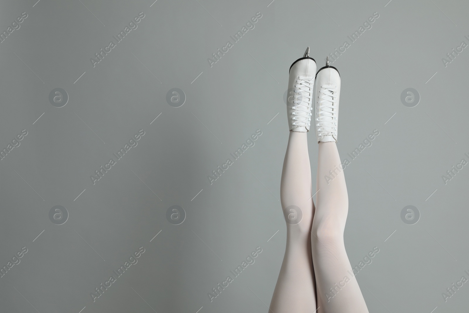 Photo of Woman in elegant white ice skates on grey background, closeup of legs. Space for text