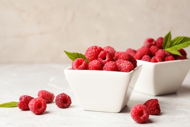 Bowls with delicious ripe raspberries on marble table against light background, space for text