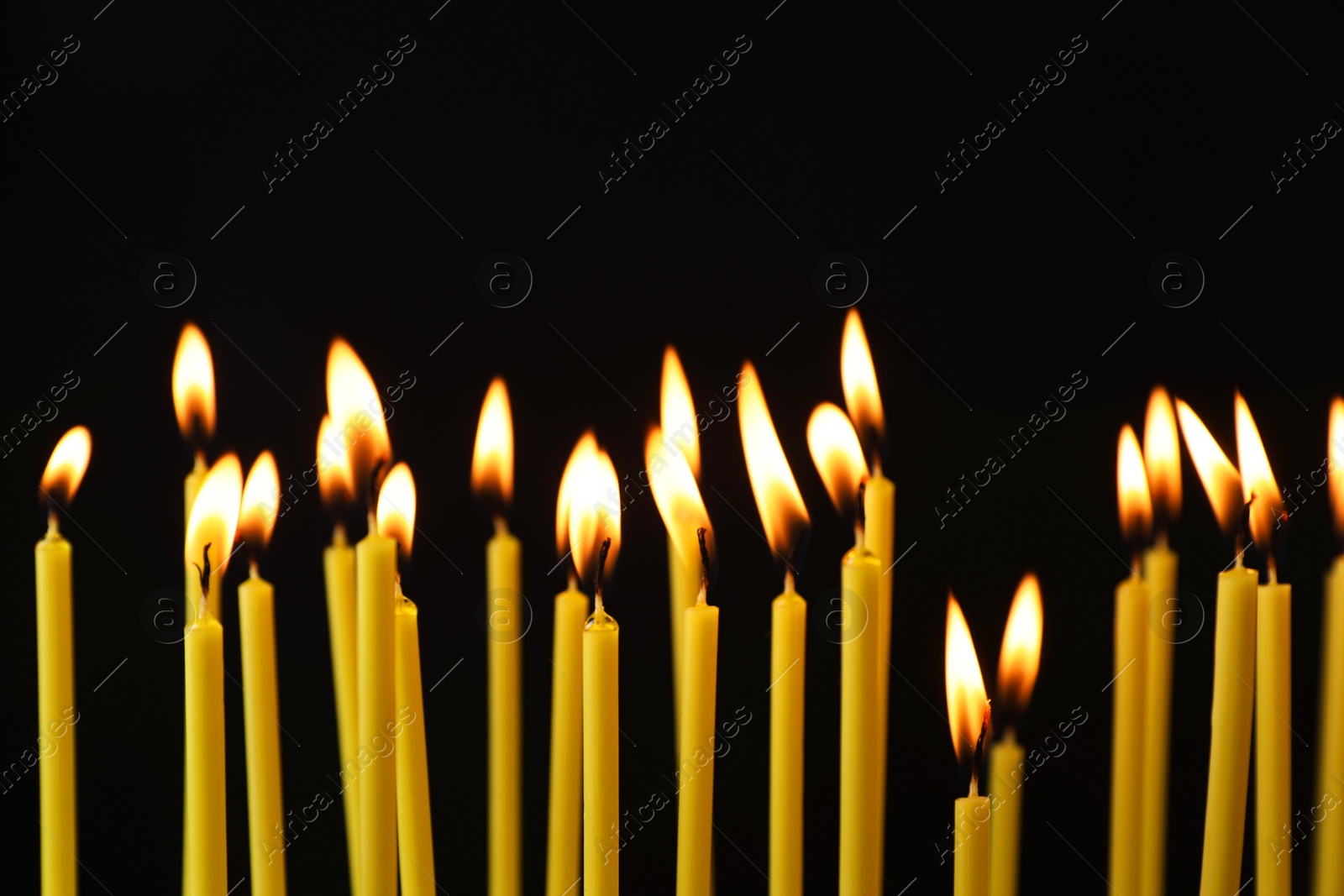 Photo of Many burning church candles on black background