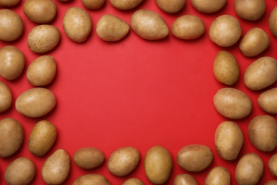 Photo of Frame made of raw fresh organic potatoes on red background, flat lay. Space for text