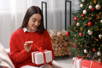 Smiling woman opening gift near Christmas tree indoors