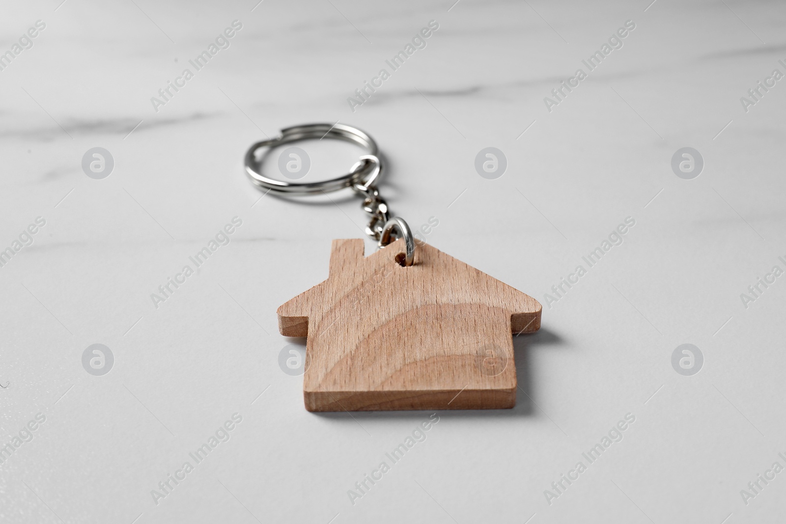 Photo of Wooden keychain in shape of house on marble table, closeup