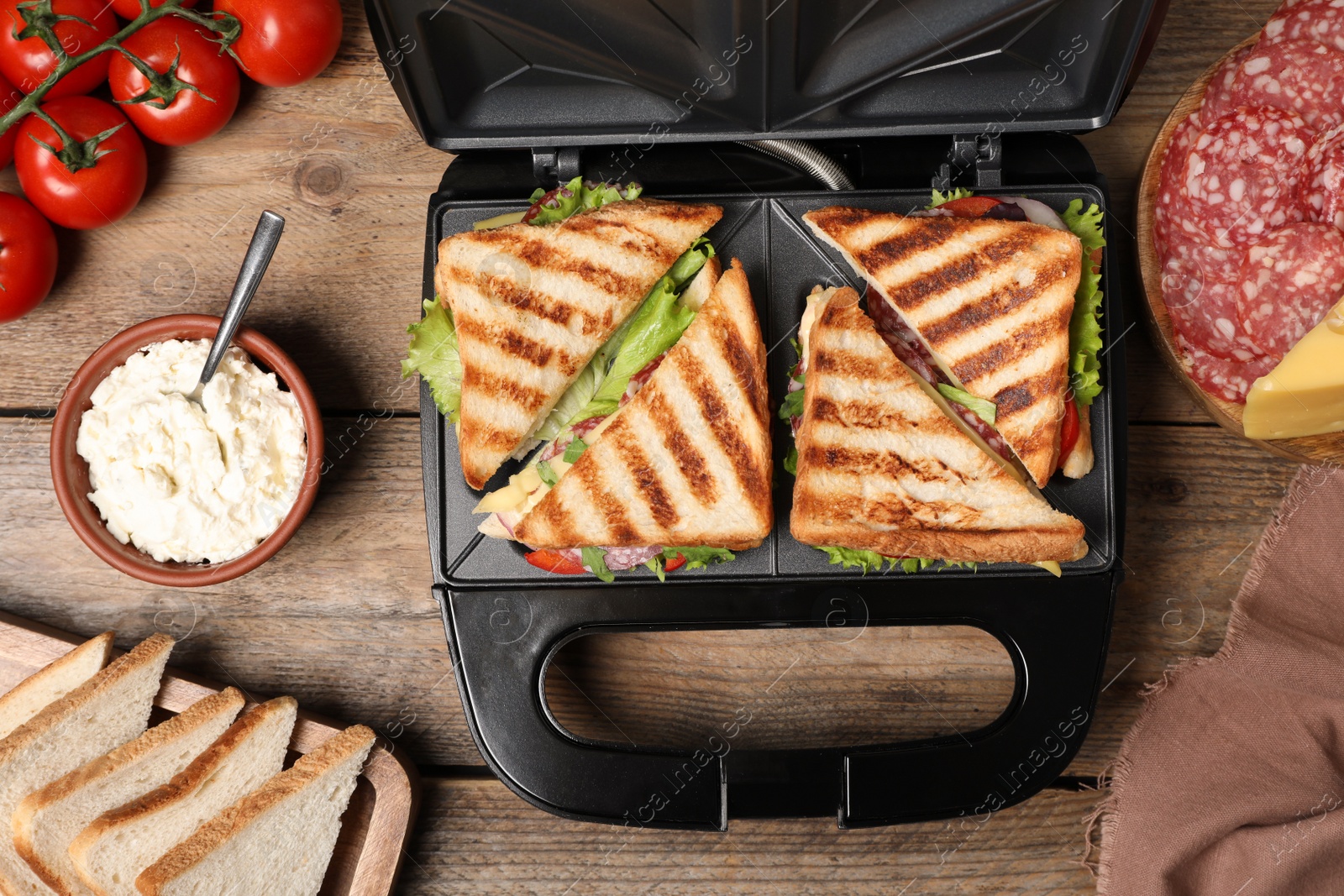 Photo of Modern grill maker with sandwiches and different products on wooden table, flat lay