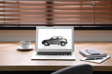 Laptop screen with automobile on wooden table. Car buying`