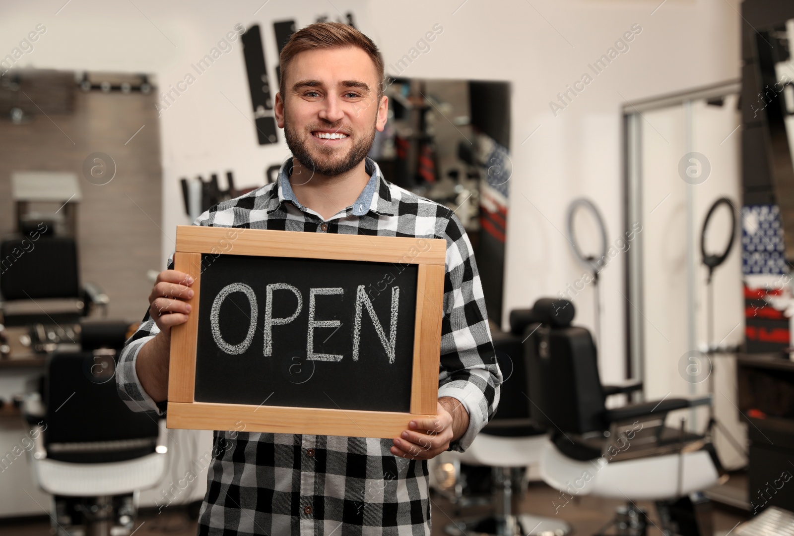 Photo of Young business owner holding OPEN sign in his barber shop