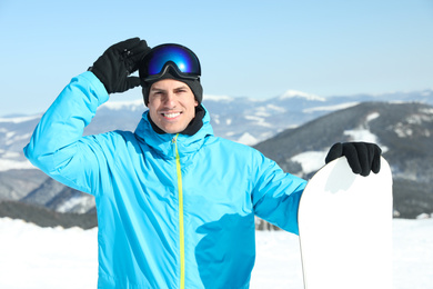 Happy man with snowboard in mountains. Winter vacation