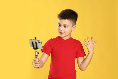Photo of Cute little blogger recording video on yellow background