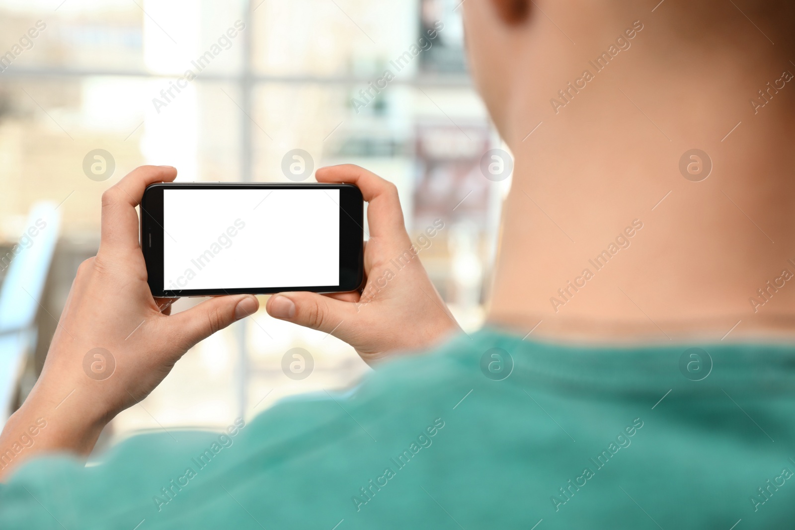 Photo of Man holding smartphone with blank screen on blurred background, closeup of hands. Space for text