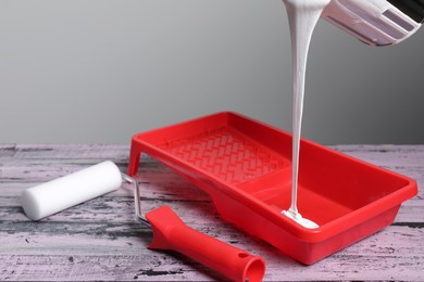 Photo of Pouring paint from can into tray on old pink wooden table