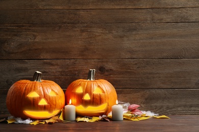 Photo of Pumpkin jack o'lanterns, autumn leaves and candles on wooden table, space for text. Halloween decor