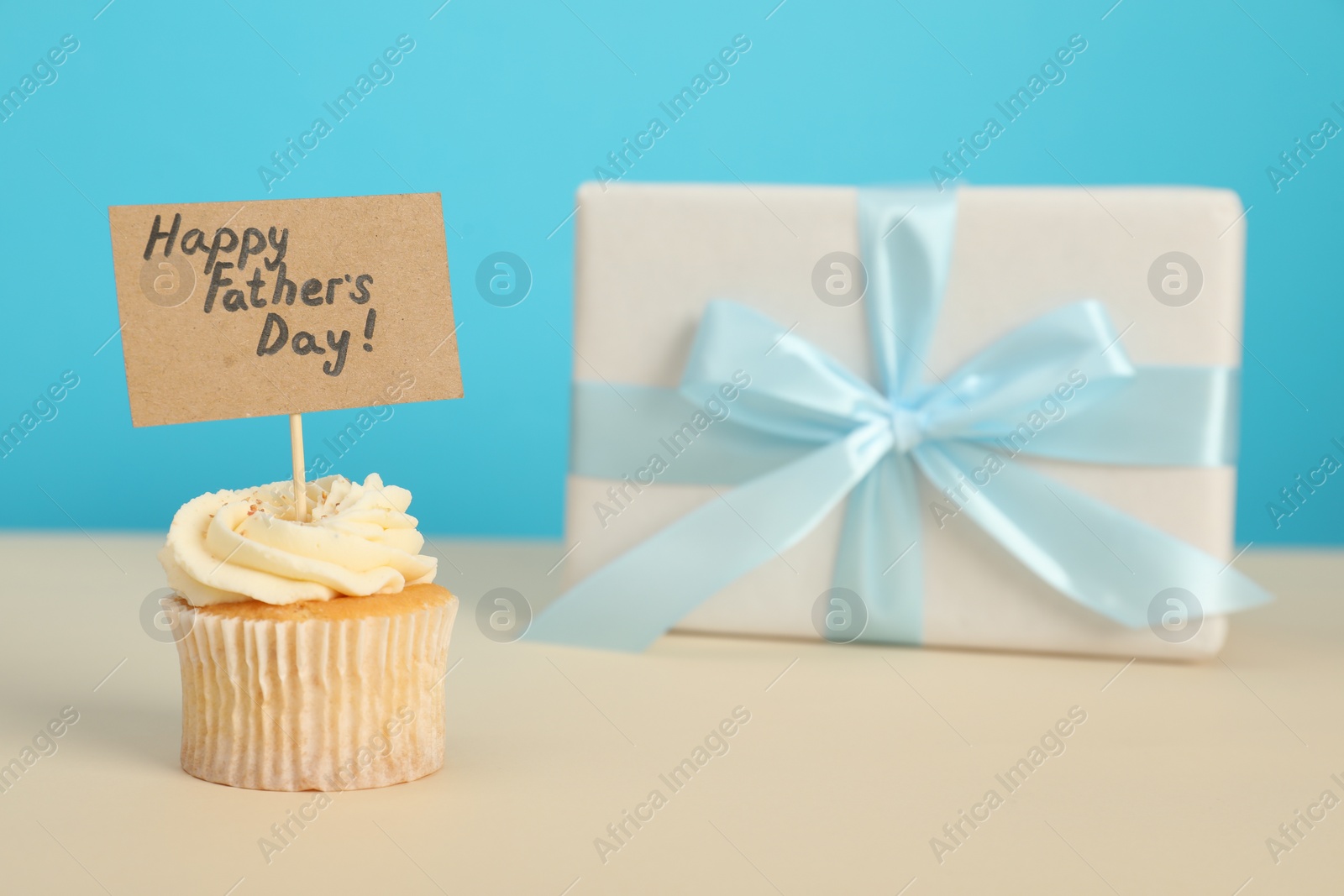 Photo of Happy Father's Day. Tasty cupcake with greetings and gift box on beige table, closeup. Space for text
