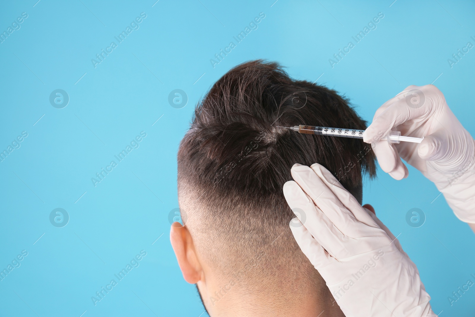 Photo of Young man with hair loss problem receiving injection on color background. Space for text