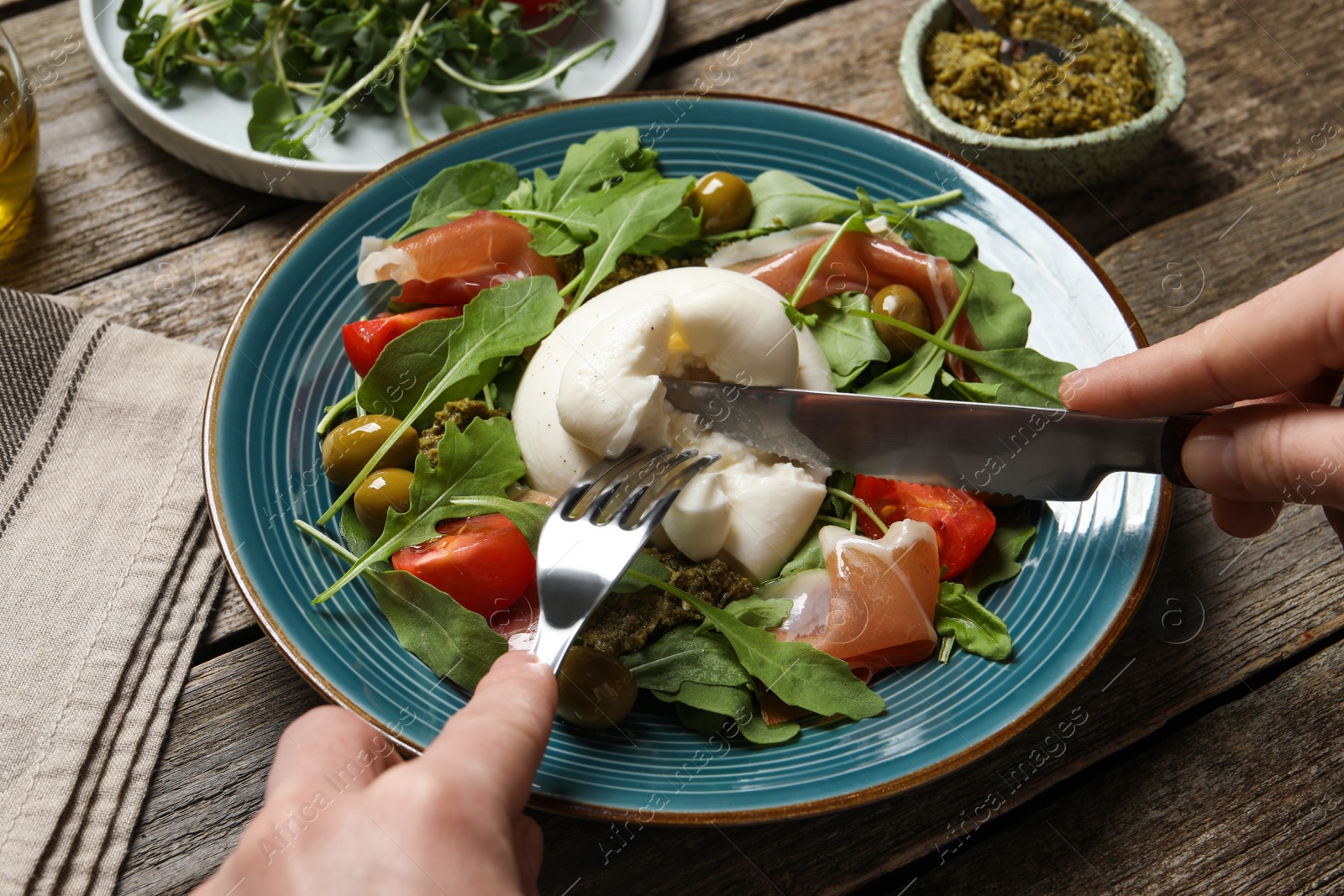 Photo of Woman eating delicious burrata salad at wooden table, closeup