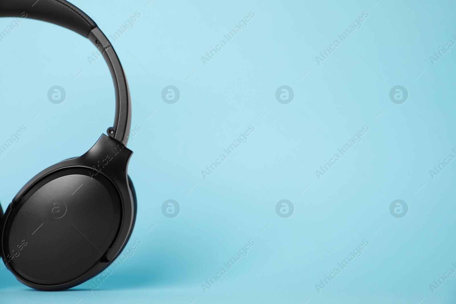 Photo of Modern wireless headphones on light blue background. Space for text