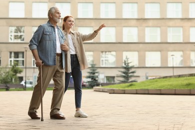 Photo of Senior man with walking cane and young woman outdoors. Space for text