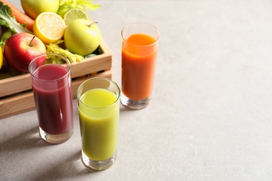 Glasses of different juices and wooden crate with fresh ingredients on table. Space for text