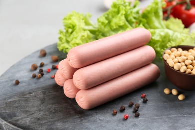 Photo of Fresh raw vegetarian sausages, lettuce and soybeans on grey board, closeup