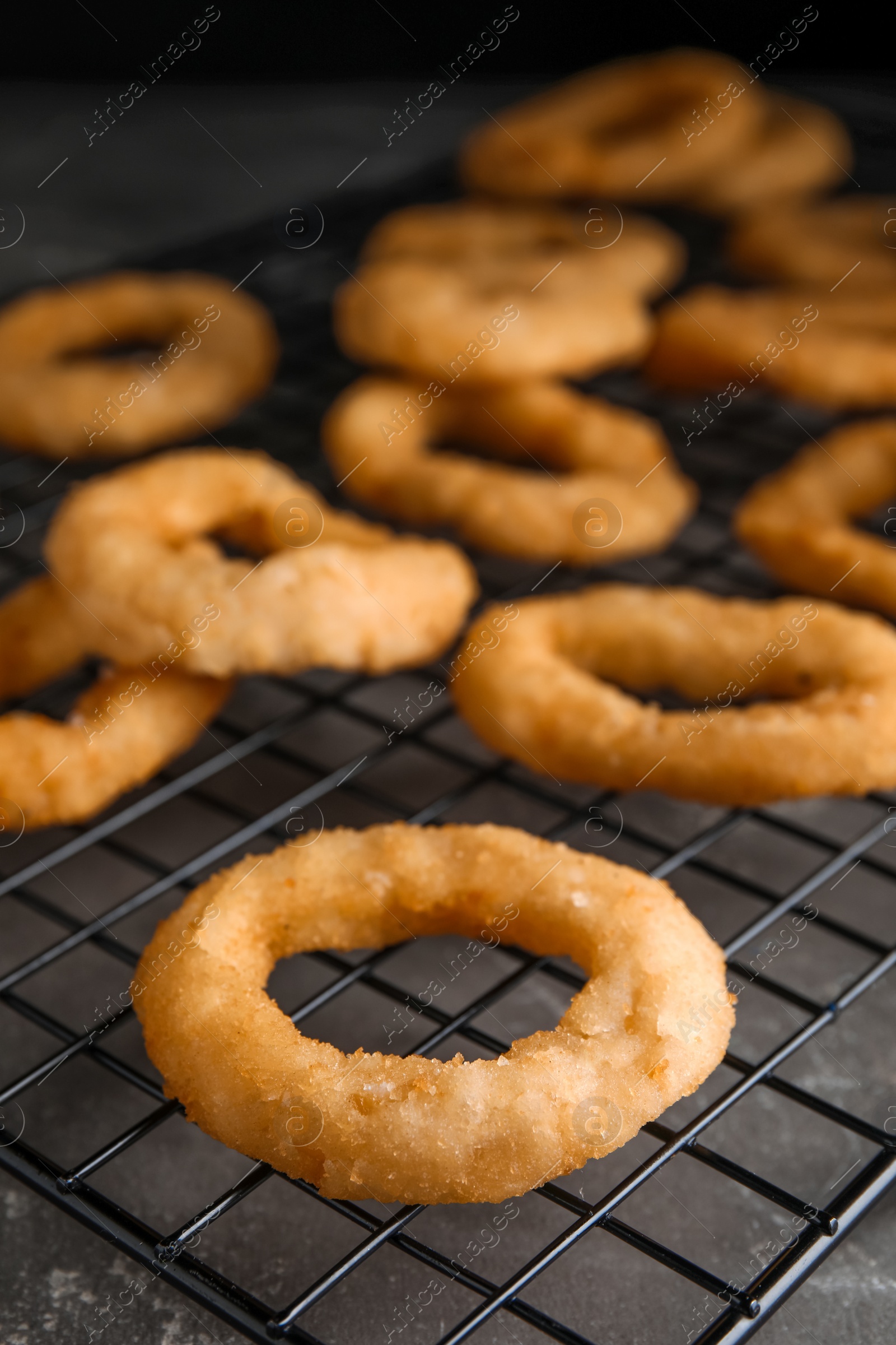 Photo of Cooling rack with fried onion rings on grey table