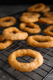 Photo of Cooling rack with fried onion rings on grey table