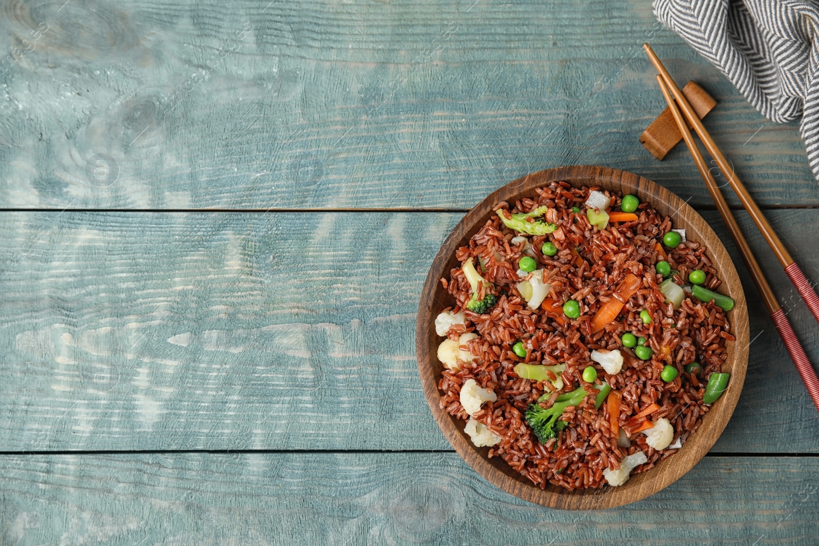 Photo of Plate of brown rice with vegetables and chopsticks on color wooden table, flat lay. Space for text