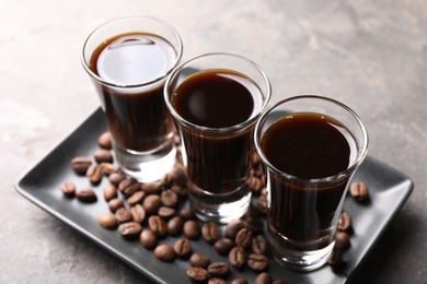 Photo of Shot glasses with coffee liqueur and beans on light grey table, closeup