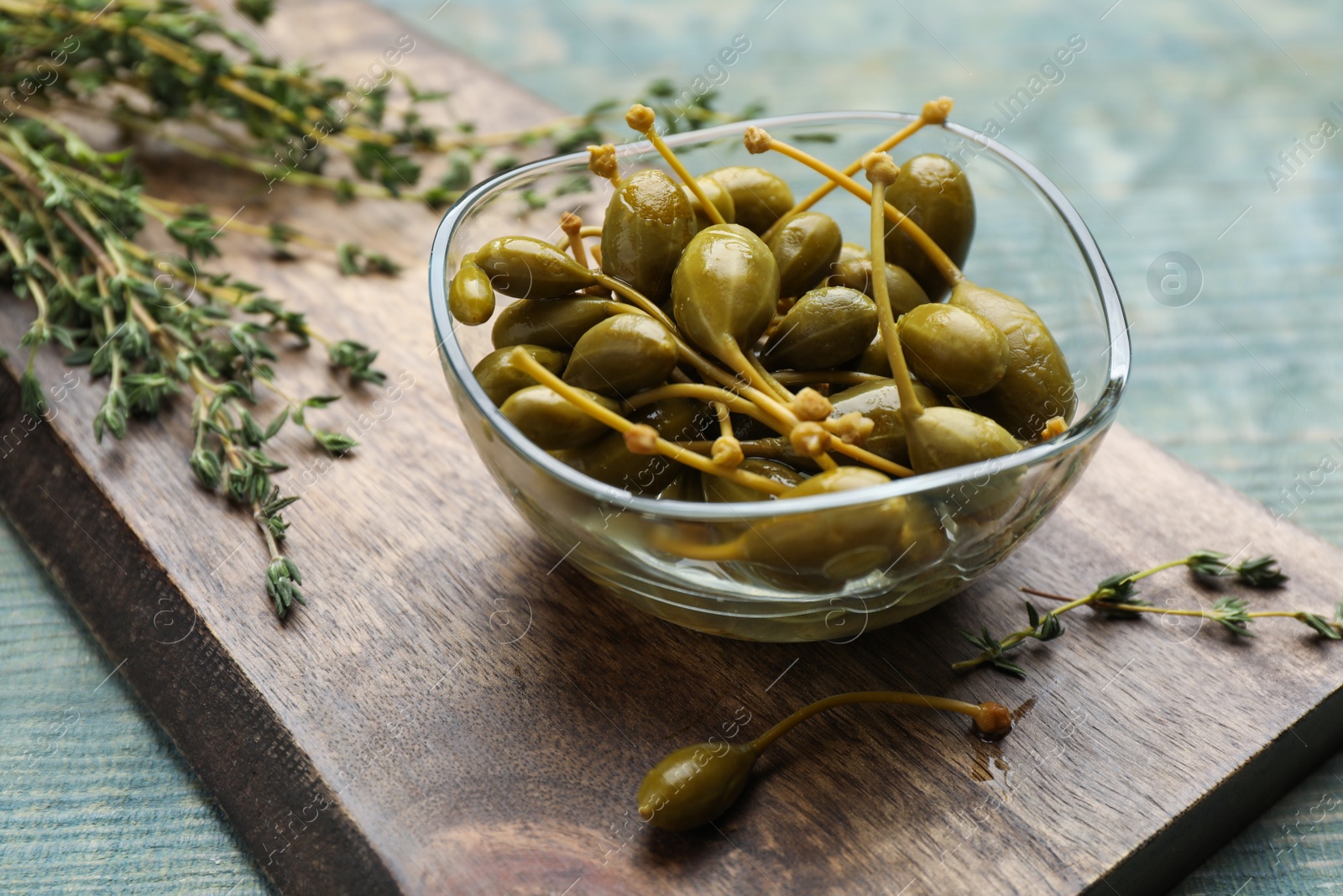 Photo of Tasty capers in glass bowl and thyme on light blue table