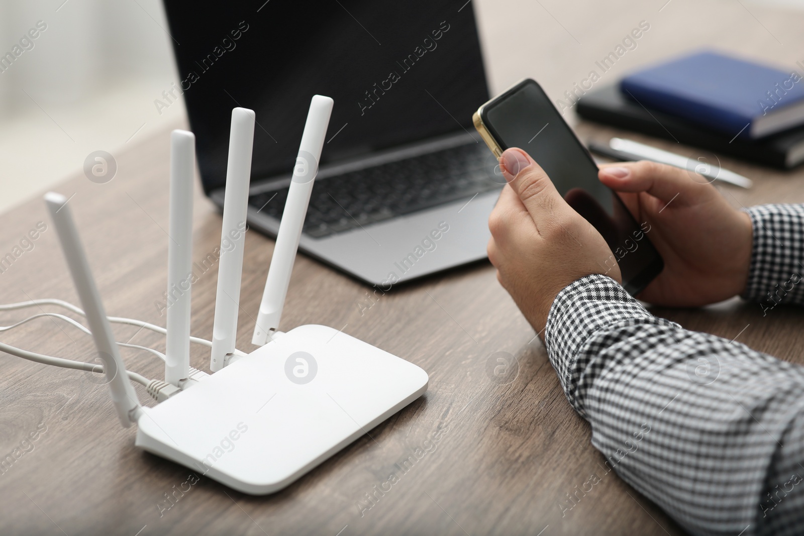 Photo of Man with smartphone and laptop connecting to internet via Wi-Fi router at wooden table, closeup